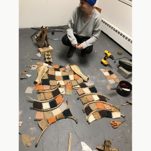 一名学生在一块由小块缝制的一件上工作,缝合在一起,挂在骨头上