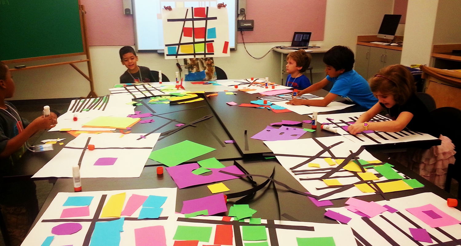一群小学生围坐在一张大桌子旁，桌子上铺满了剪纸、彩色的图画纸。