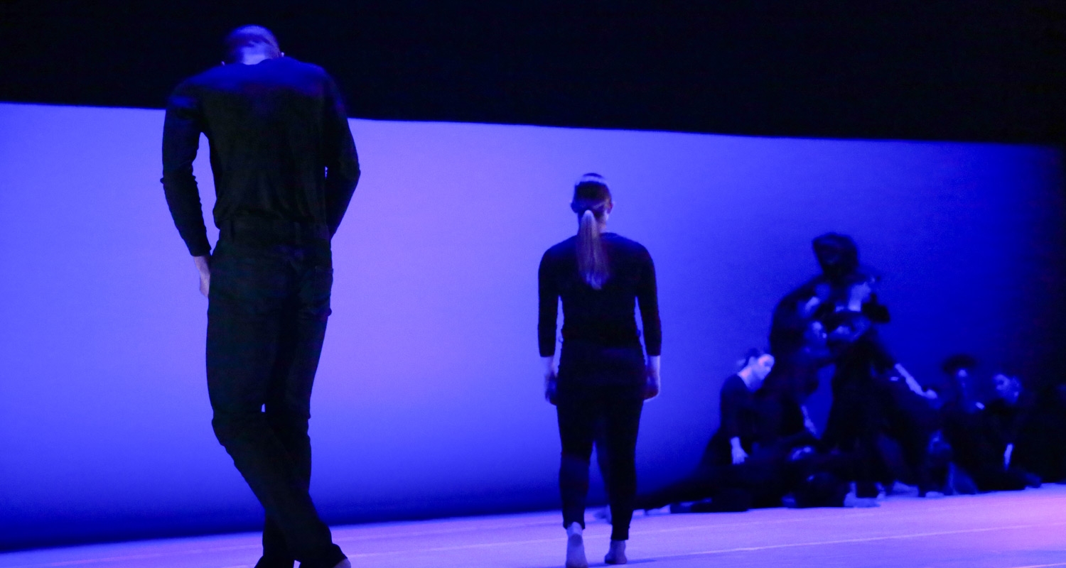 舞蹈学生身着黑色服装，以蓝色和紫色为背景在舞台上表演