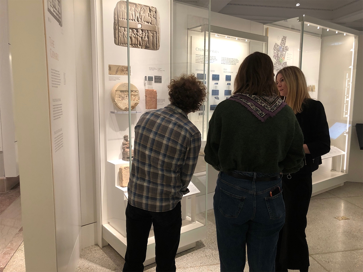 两个学生一边听导游讲解，一边看宾州博物馆的一件文物。
