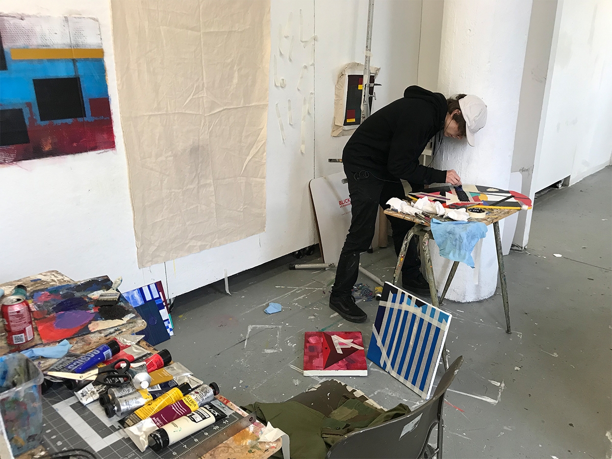 学生在他们的绘画工作室工作在一件艺术品。涂料布置在桌子上，并抵靠墙壁进行帆布。