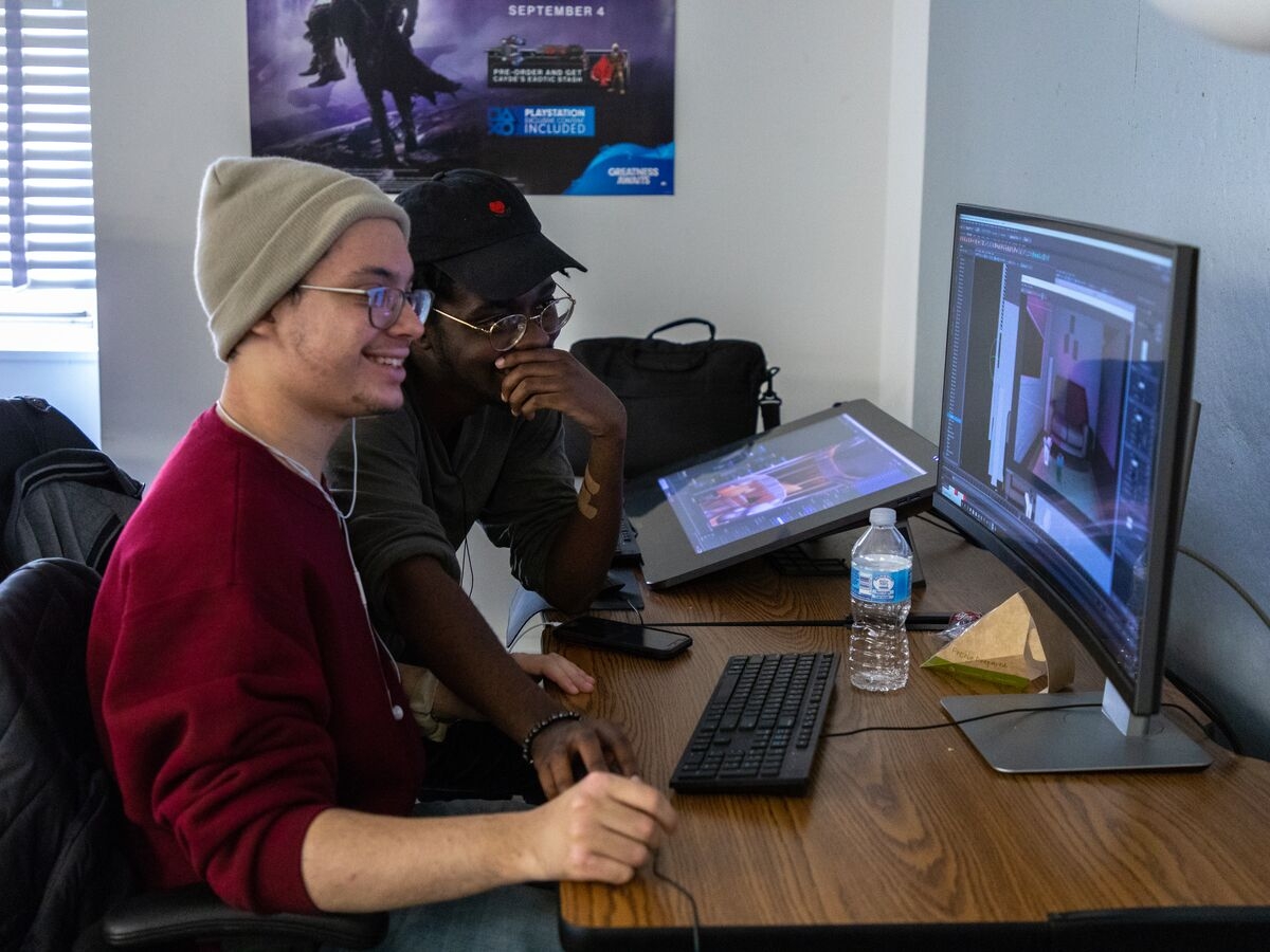 两个学生一起使用计算机和平板电脑在游戏艺术计划中创建动画项目。