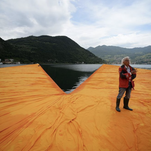 一个人站在一块漂浮在湖面上的巨大的橙色床单上＂typeof=