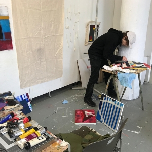 一名学生在画室里创作一件艺术品。油漆铺在桌子上，画布靠墙支撑。