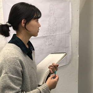 一名学生一边做笔记，一边检查一件艺术品。
