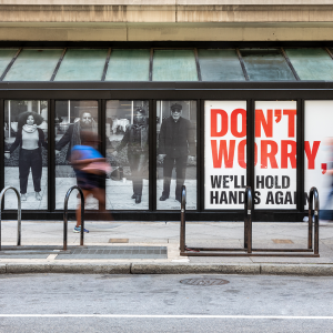 一块广告牌上，人们手牵着手，用红色字体写着“别担心，我们还会再牵手的”。
